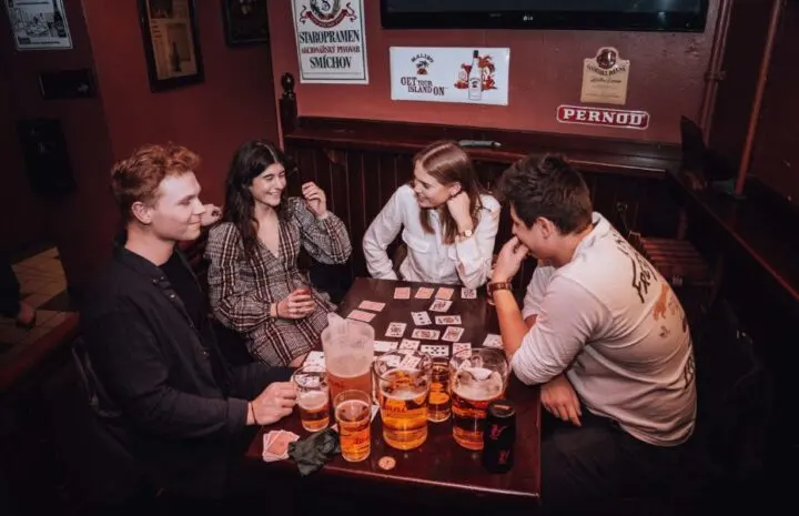 Gruppe venner spiller drukspil med kort og øl ved et bord